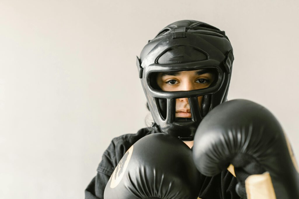 A focused young martial artist wearing protective helmet and gloves, ready to train. Indoors setting.