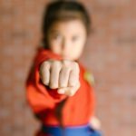 Child in martial arts uniform performs a focused punch indoors.