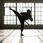 Martial artist performing a high kick in a sunlit room creating dramatic shadows.